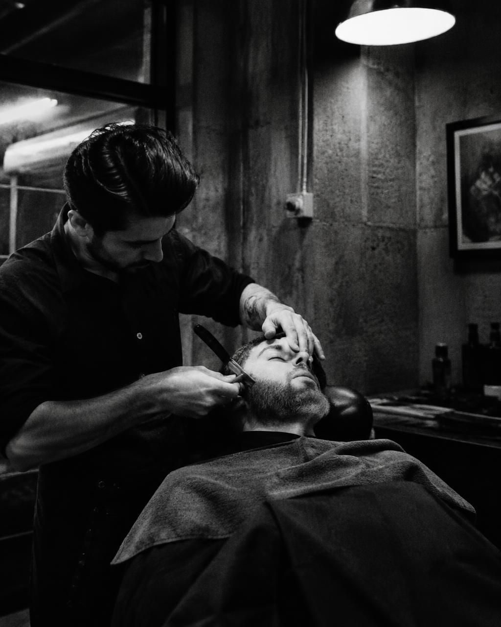 Barber shaping a client's beard with a straight razor